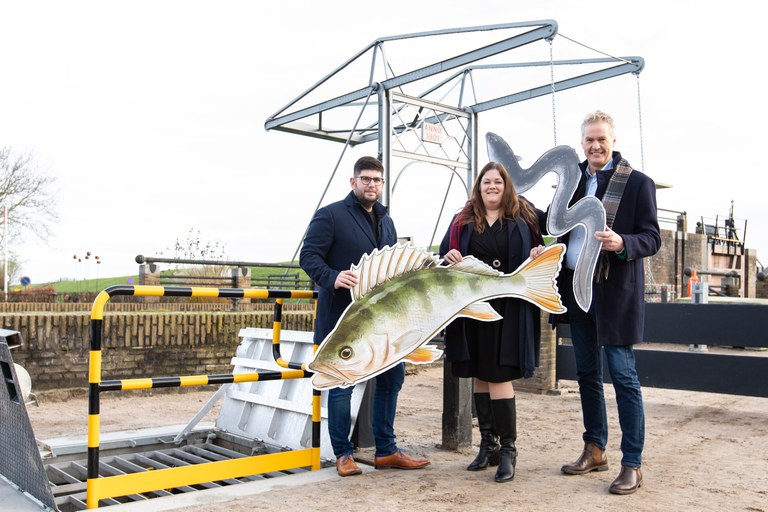 (V.l.n.r.) gedeputeerde Sijbe Knol (provincie Fryslân), wethouder Rebecca Slijver (gemeente Noardeast-Fryslân) en dagelijks bestuurslid Gerben de Boer (Wetterskip Fryslân) openen de nieuwe vispassage in Ezumazijl door symbolisch de vissen de ruimte te geven. Foto: Marit Anker.